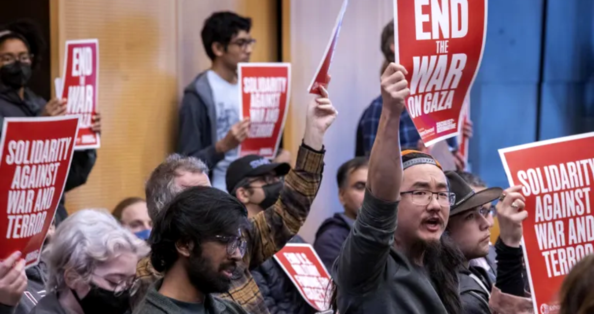 Protestors at a city council meeting hold signs reading "End the War on Gaza" and "Solidarity Against War and Terror"
